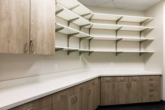 This image of the pharmacy and storage wall at Montclair Animal Clinic shows open storage shelves, light wood cabinetry, white counters, and organized veterinary clinic supplies.