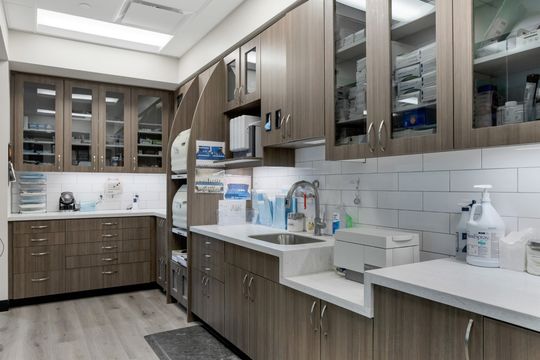 This image of the sterilization and storage wall at Soult and Swanson Family Dentistry shows glass-front cabinets, sink stations, countertop equipment, and organized dental supplies.