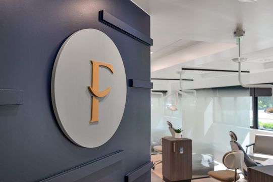 The Foundations Orthodontics logo wall viewed alongside the modern clinical treatment space and glass partitioned rooms.