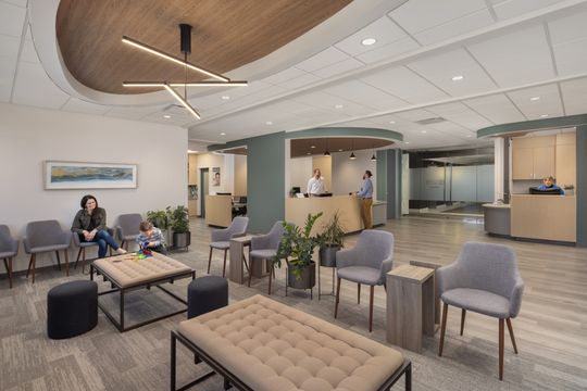 This image of the waiting lounge with patients at Core Dermatology shows lounge seating, people seated in the waiting area, side tables, and curved ceiling feature.