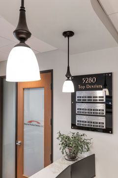 An entry detail at Bridge Creek Dentistry featuring a glass office door, pendant lighting, interior directory sign, plant decor, and clean contemporary finishes.