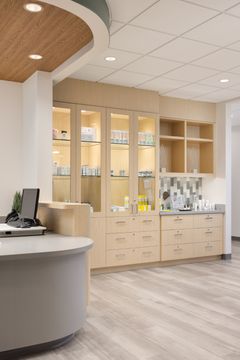 This image of the display cabinet and reception detail at Core Dermatology shows wood product display cabinets, curved reception edge, skincare shelves, and bright lobby lighting.