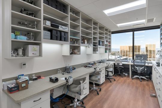 A long view of the Bridge Creek Dentistry lab and supply workspace with open shelving, counters, dental tools, workstations, and large windows with city views.