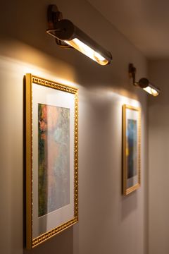 This image of the framed art hallway detail at Collective Health shows framed wall art, brass picture lights, neutral walls, and warm corridor lighting.