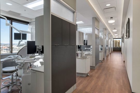 A clean clinical hallway at Bridge Creek Dentistry with treatment rooms, wood flooring, modern cabinetry, large windows, and a bright organized dental office layout.