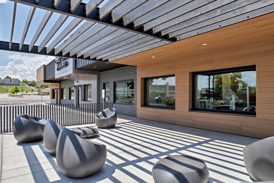 A closer exterior view of Arvada Dental Center & Implants featuring the covered patio area, outdoor seating, modern pergola structure, wood-look facade, and views into the dental treatment rooms.