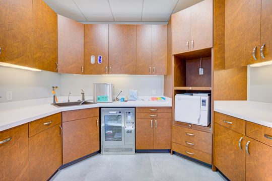 This image of the sterilization lab cabinetry at Meridian Periodontics of Central Park shows wood cabinetry, white counters, sink, sterilization equipment, and organized clinical storage.