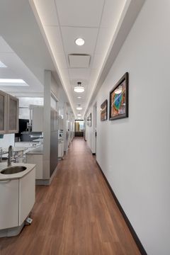 A long clinical hallway at Bridge Creek Dentistry featuring wood flooring, treatment room access, modern wall art, bright lighting, and a clean professional layout.