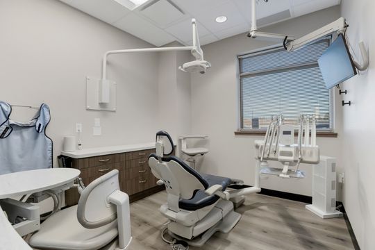 This image of the bright dental operatory at Soult and Swanson Family Dentistry shows a dental chair, overhead equipment, window shade, sink cabinet, and clean treatment room finishes.
