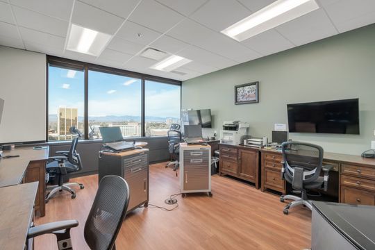 A private consultation office at Bridge Creek Dentistry featuring desks, chairs, storage cabinets, wall-mounted display, large window, and mountain views.