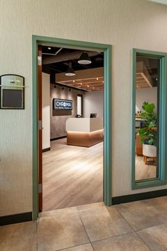 This image of the interior entry hallway at Chroma Dental Studio shows green-trimmed doorways, wood flooring, mirrored wall detail, and a view into the reception area.