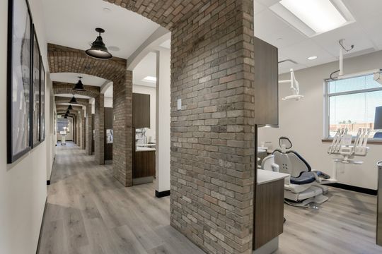 This image of the brick hallway and operatory view at Soult and Swanson Family Dentistry shows brick archway, long corridor, treatment rooms, dental chairs, and wood-look flooring.