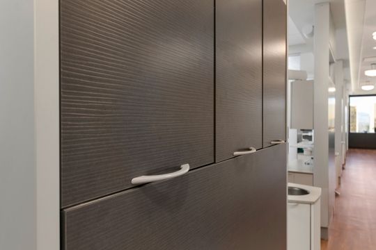 A detailed interior view at Bridge Creek Dentistry showing dark textured cabinetry, a bright clinical hallway, wood flooring, and clean modern treatment room design.