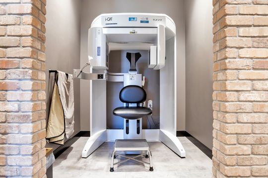 An advanced imaging area at Arvada Dental Center featuring an i-CAT dental scanning system, patient chair, protective apron, brick accent walls, and a clean diagnostic setting.