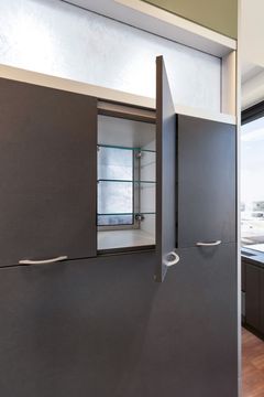 A detailed view of open storage cabinetry at Bridge Creek Dentistry with dark textured doors, glass shelving, frosted transom window, and modern clinical storage design.
