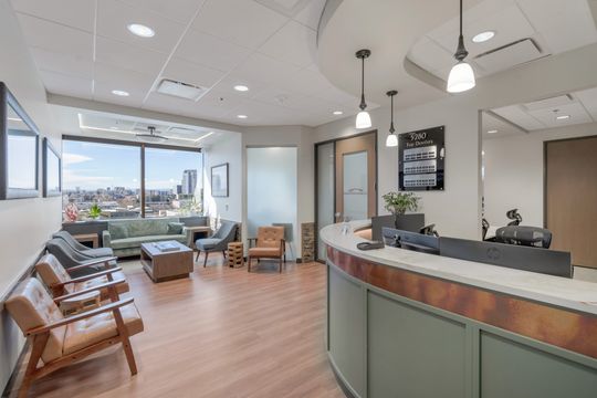 A spacious waiting room and reception area at Bridge Creek Dentistry with wood seating, pendant lights, large windows, front desk, and warm contemporary finishes.