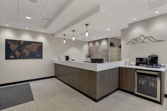 This image of the reception counter wide view at Soult and Swanson Family Dentistry shows a long wood front desk, coffee station, wall art, pendant lights, and clean waiting room layout.