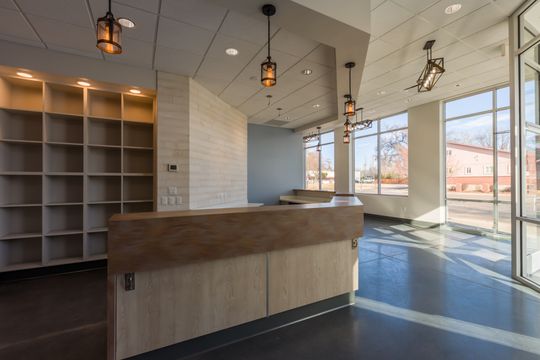 This image of the front desk and retail shelving at Montclair Animal Clinic shows a reception desk, open shelving, pendant lights, blue accent wall, and large storefront windows.