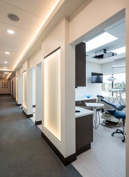 This image of the clinical hallway and operatory access at Collective Health shows treatment room openings, wall panels, bright ceiling lights, and clean dental office circulation.
