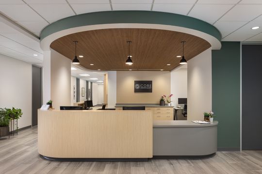 This image of the curved reception desk view at Core Dermatology shows a wood reception counter, branded wall sign, green accent wall, and rounded ceiling feature.