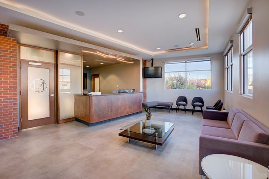 This image of the reception lobby with seating at Meridian Periodontics of Central Park shows a reception desk, purple bench seating, coffee table, waiting chairs, and large windows.