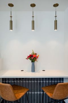 A modern counter area at Foundations Orthodontics featuring pendant lighting, dark tile, leather chairs, and a floral arrangement.