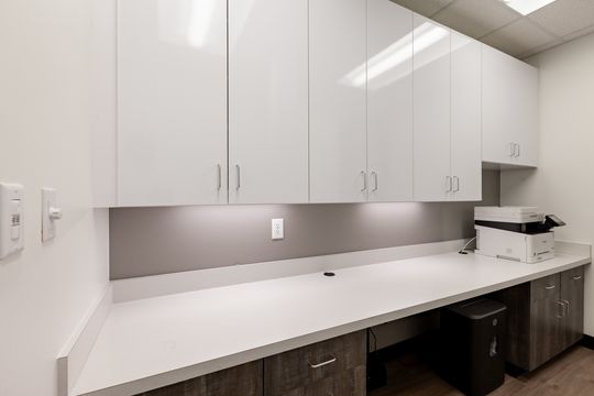 This image of the white clinical cabinetry wall at Chroma Dental Studio shows upper cabinets, long white countertop, open knee spaces, outlets, and bright task lighting.