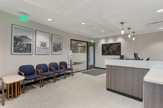 This image of the waiting room and front desk view at Soult and Swanson Family Dentistry shows blue seating, framed wall art, reception counter, coffee station, and bright lobby ceiling.