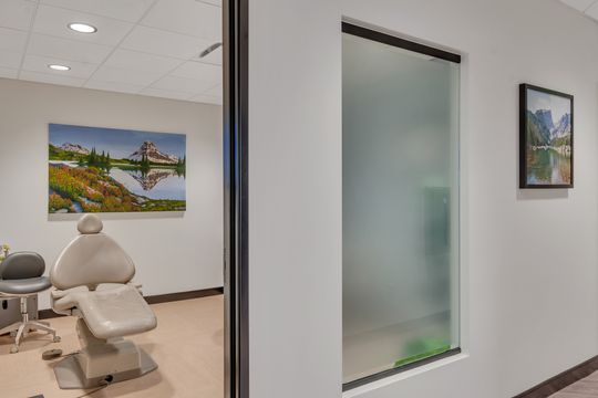 A view into a private Foundations Orthodontics treatment room featuring a dental chair, glass entry, and colorful mountain artwork.
