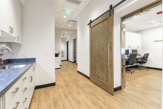 A clinical hallway at Elevation Dermatology showing cabinetry, wood flooring, and a sliding barn-style door leading into an office space.