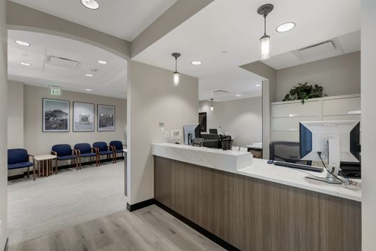 This image of the reception desk interior view at Soult and Swanson Family Dentistry shows front desk workstations, blue waiting chairs, pendant lights, and framed wall art.