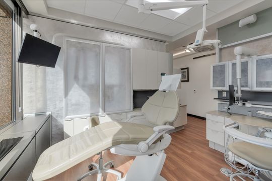 A clean and comfortable treatment suite at Bridge Creek Dentistry featuring a dental chair, overhead equipment, large window, neutral finishes, and organized clinical cabinetry.