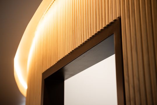 This image of the curved wood wall detail at Collective Health shows vertical wood slats, curved accent lighting, doorway trim, and warm contemporary finishes.
